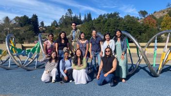 Group of smiling adults posing at playground with double helix metal sculptures, sunny day